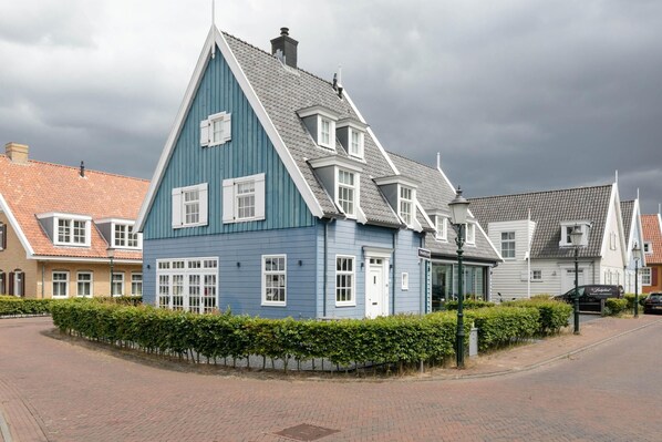 A traditional Dutch house with a steep gable roof, a small porch, and a brick pathway leading to the entrance.