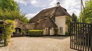 A traditional house with a thatched roof, a gravel driveway, and a black metal gate. - Cottage mouse (Hoofddorp)