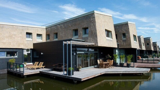 A modern waterfront property with a glass-enclosed patio, outdoor seating, and a dock extending into the water. - Cottage mouse (Hoofddorp)