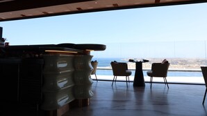 A modern interior with a bar area, two chairs, and a large window offering a view of the city and coastline. - Luxury High Floor Suite Mercury Towers (St. Julian's)