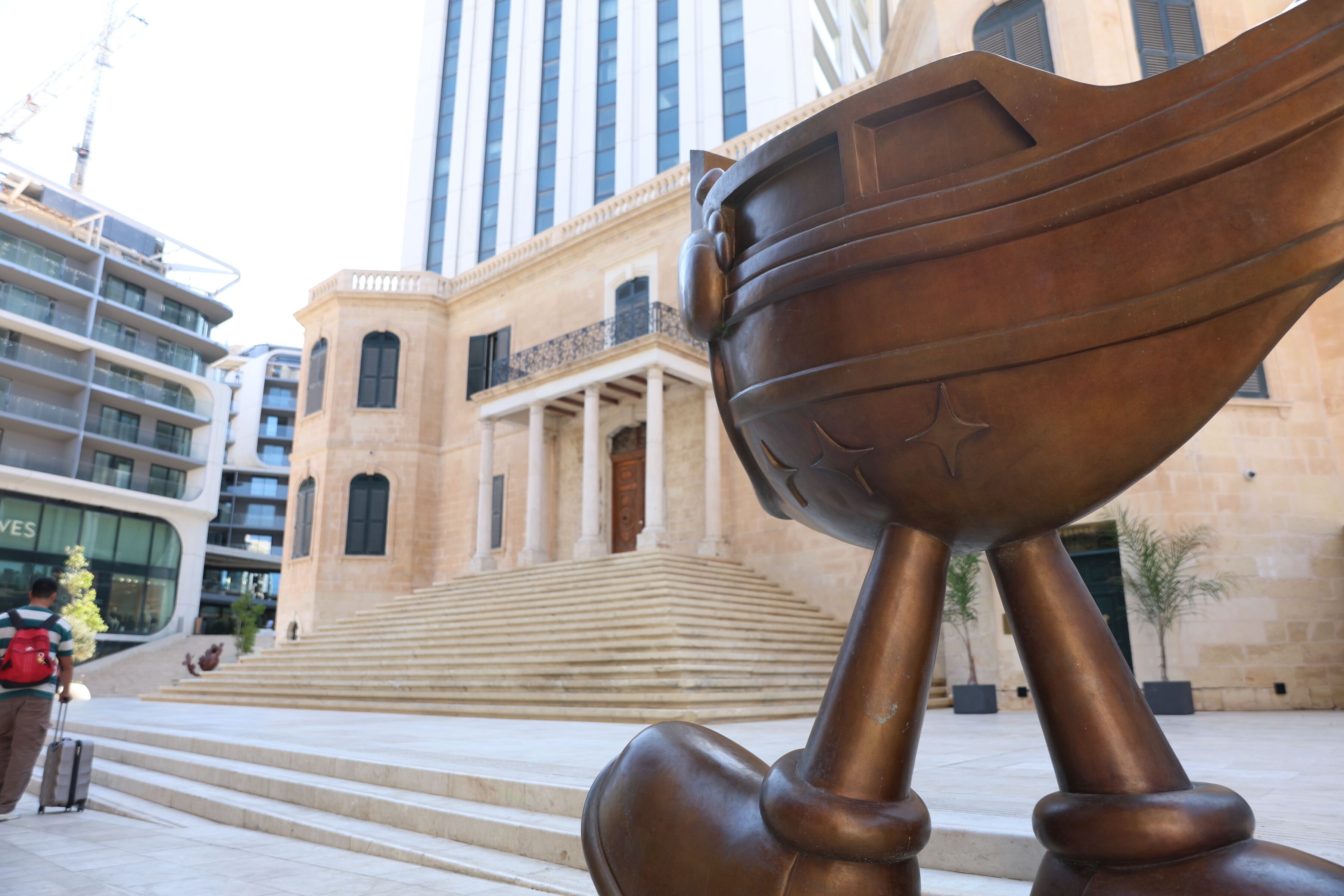A bronze sculpture of a hand holding a bowl in front of a building with steps leading to a door.