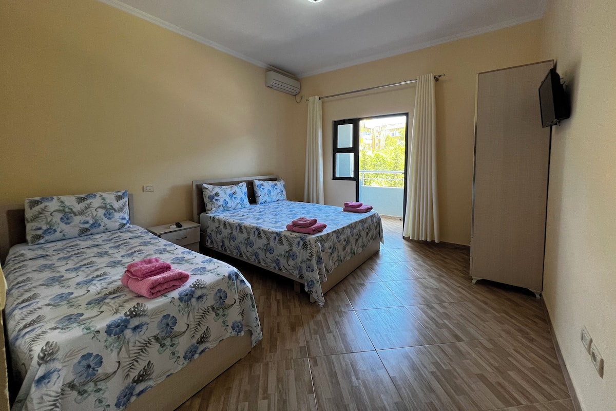 A hotel room with two beds, a wardrobe, a TV, and a window with curtains.