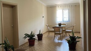 A spacious room with a wooden floor, a dining table with chairs, and several potted plants. - Canary Hotel (Golem)