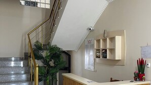 A reception area with a wooden counter, a staircase with a golden railing, and a potted plant. - Canary Hotel (Golem)