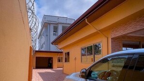 A building with a yellow facade, a garage door, and a parked car. - House - Sleeps 10 - Parking - Airport Close (Accra)