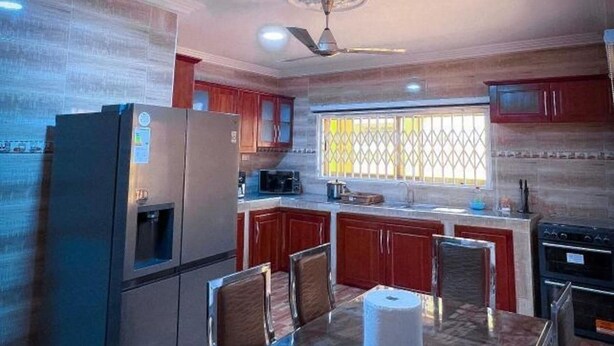A kitchen with a refrigerator, stove, microwave, and dining table with chairs. - House - Sleeps 10 - Parking - Airport Close (Accra)