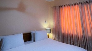 A hotel room with a bed, a nightstand, a lamp, and a window with curtains. - House - Sleeps 10 - Parking - Airport Close (Accra)