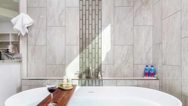 A modern bathroom with a freestanding bathtub, a wooden tray with a glass of wine, and a towel hanging on the wall. - Pecan Valley Paradise  (Hurricane)