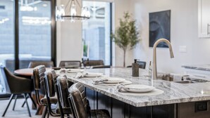 A modern kitchen with a marble countertop, stainless steel faucet, and a dining area with leather chairs. - Pecan Valley Paradise (Hurricane)