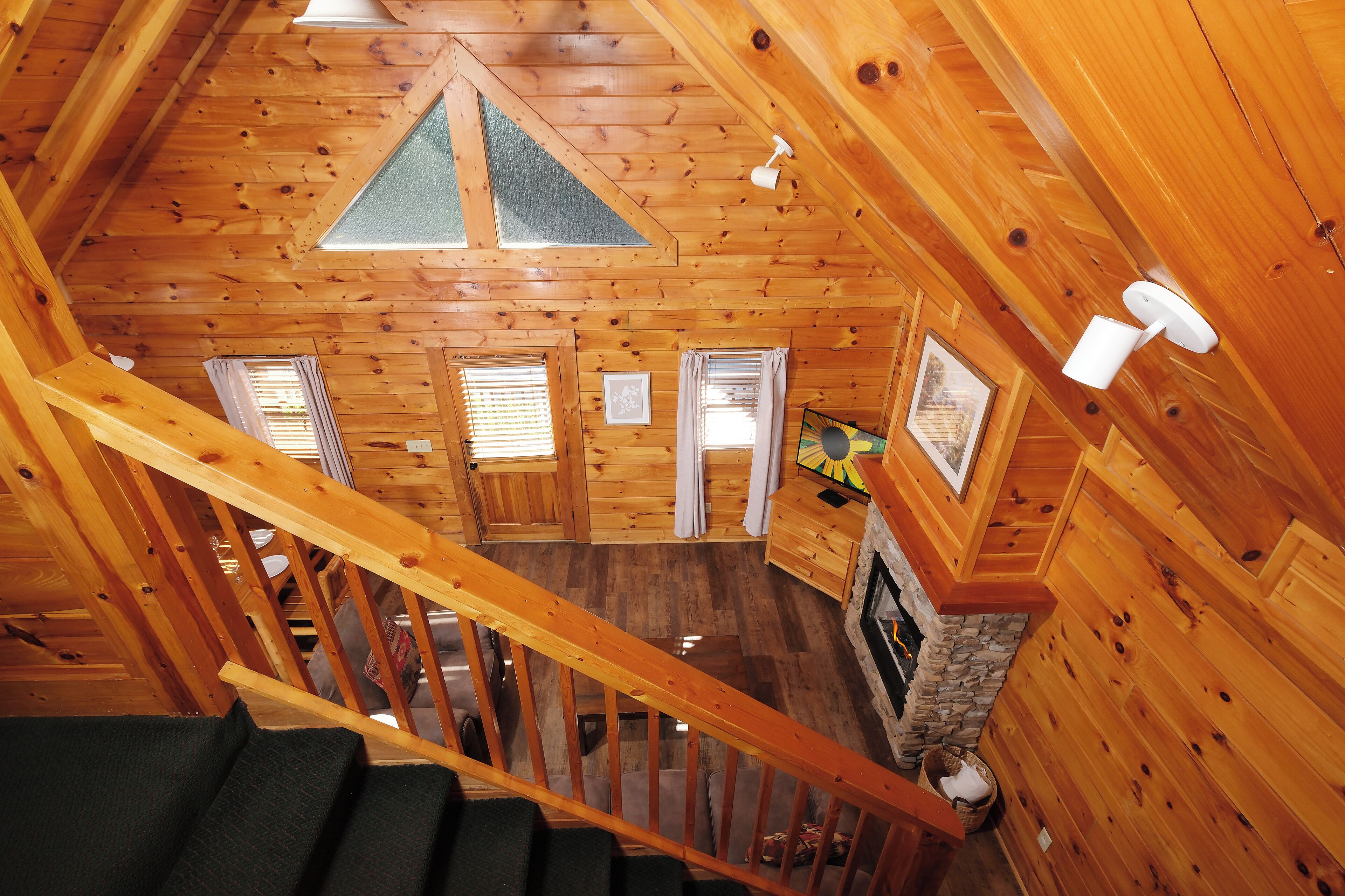 A wooden cabin interior with a staircase, a stone fireplace, and a triangular skylight.