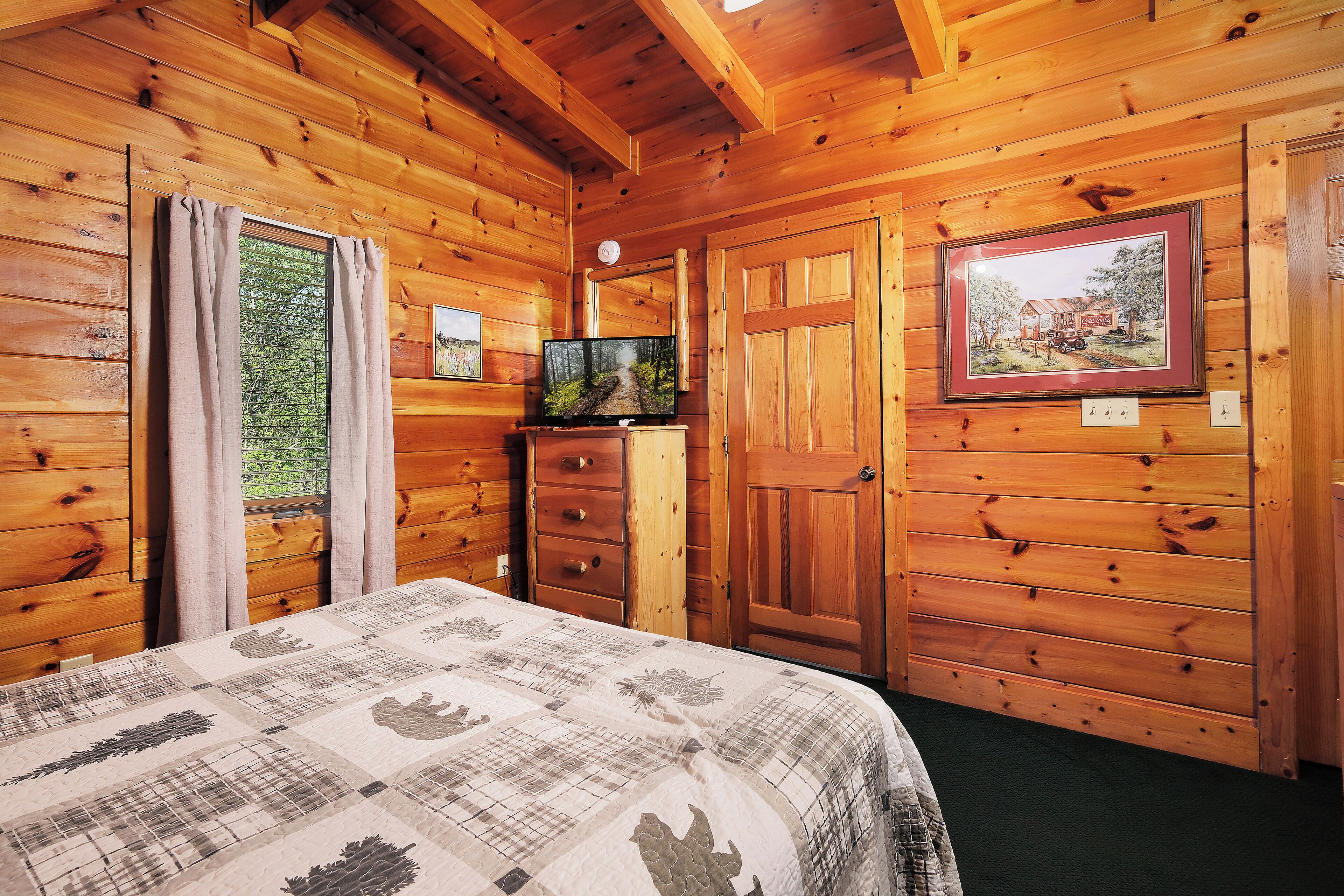 A wooden cabin room with a bed, a dresser, a television, and a framed picture on the wall.