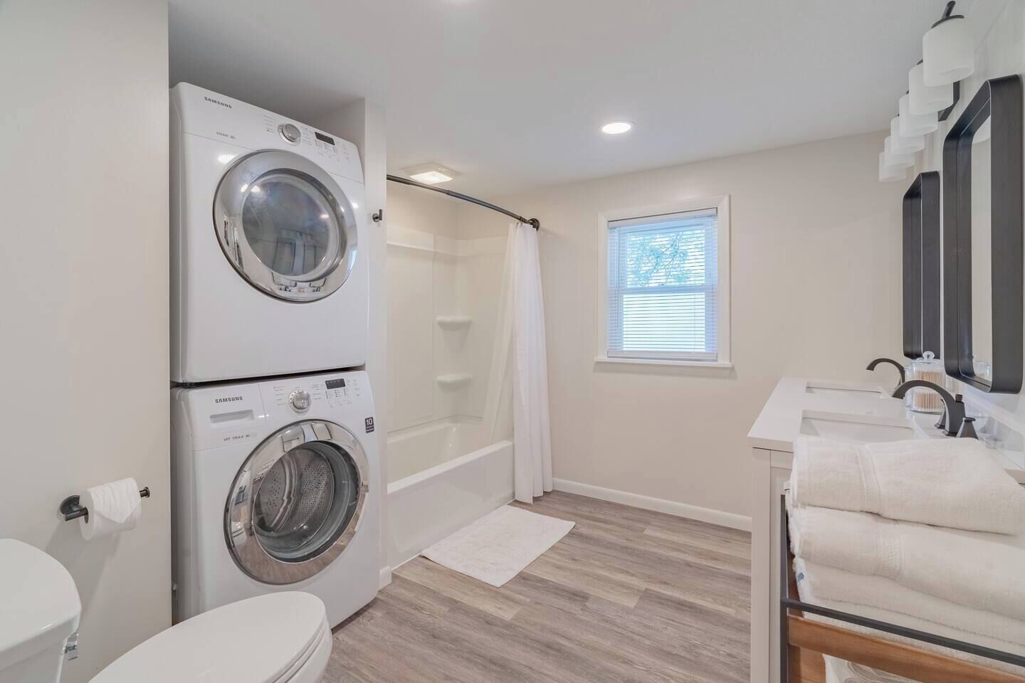 A modern bathroom with a double washer and dryer, a walk-in shower, a toilet, and a sink with a mirror.