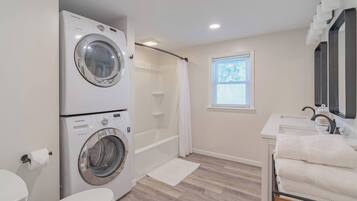A modern bathroom with a double washer and dryer, a walk-in shower, a toilet, and a sink with a mirror.