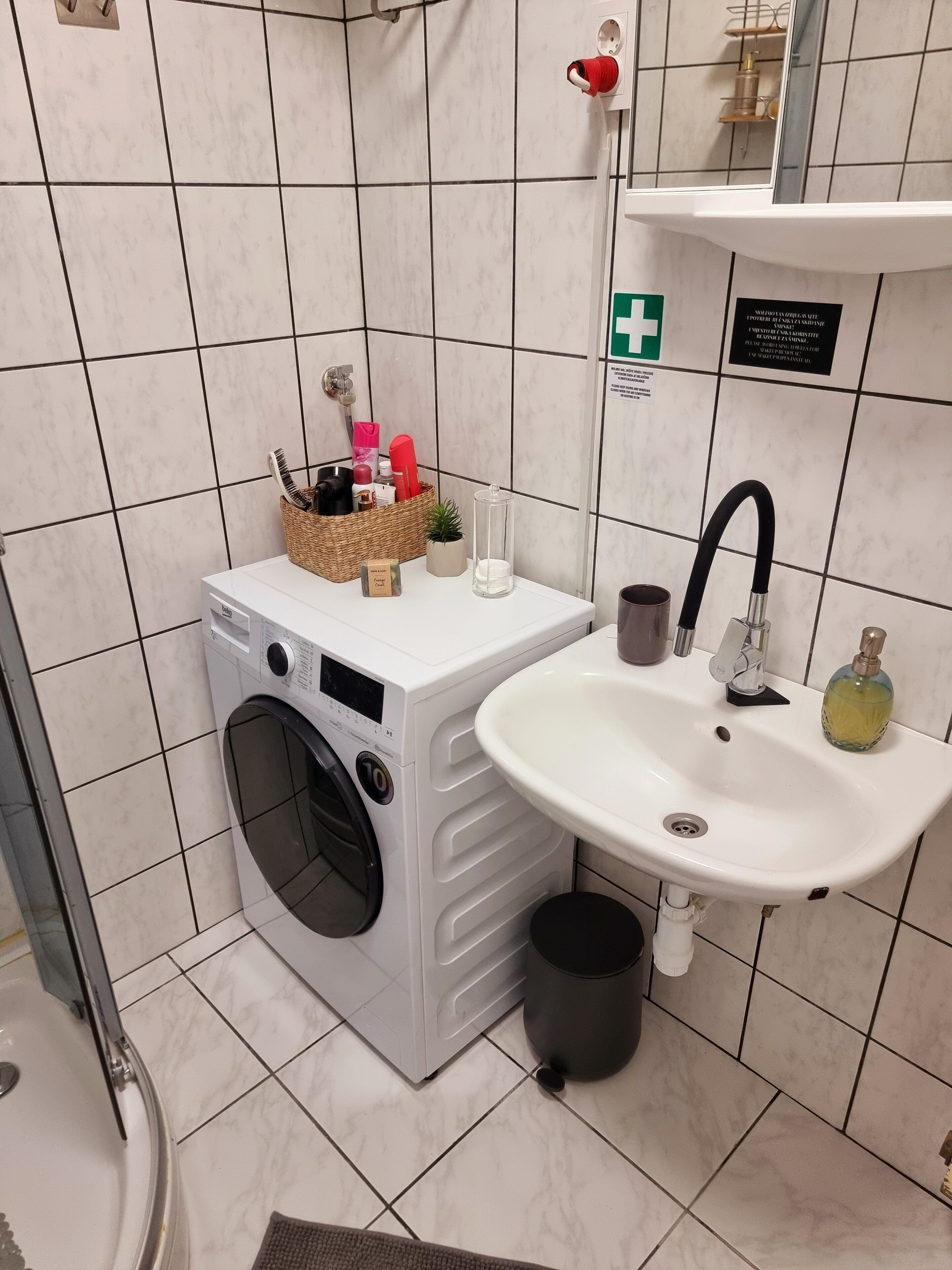 Une salle de bain équipée d’un lave-linge, d’un lavabo et d’une petite étagère où sont rangés les articles de toilette.