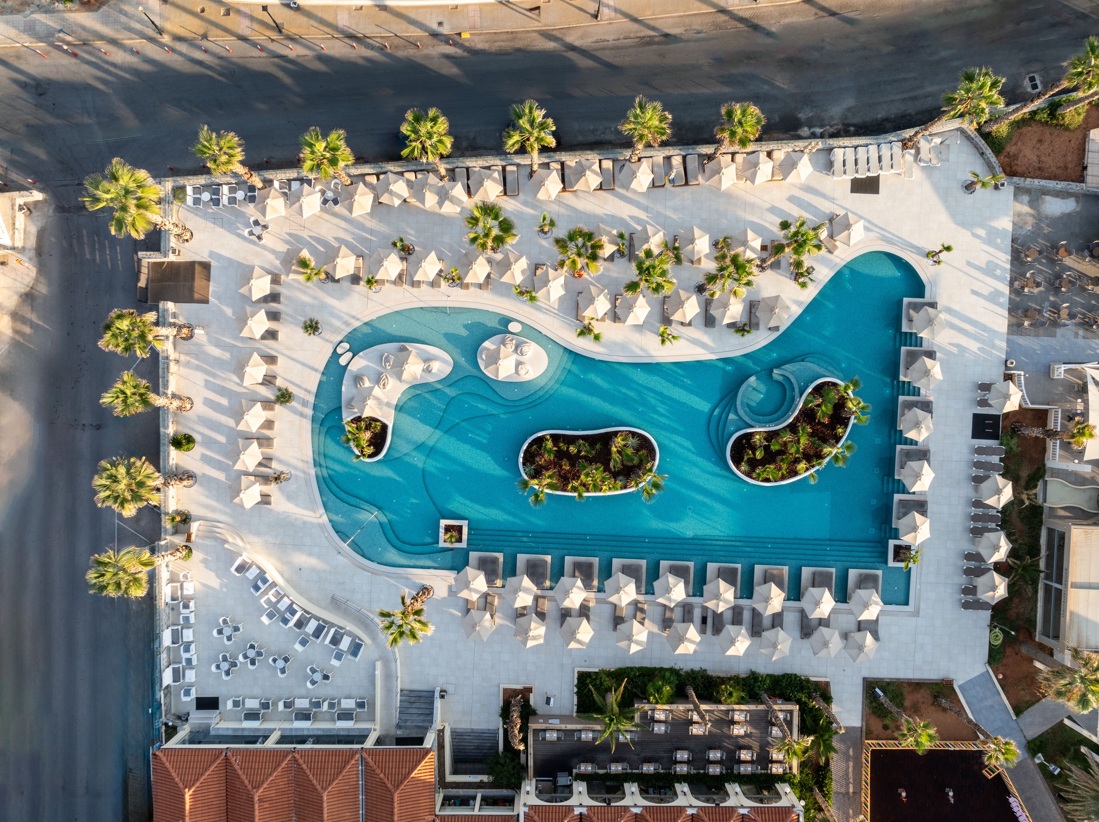 An aerial view of a resort with a large pool, sun loungers, and palm trees.