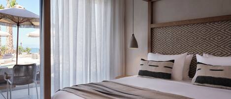 A hotel room with a large bed, a view of the sea, a balcony with outdoor seating, and a patterned headboard.