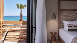 Habitación con una cama de madera, una mesita de noche de madera, una lámpara colgante y vista al océano con una palmera.