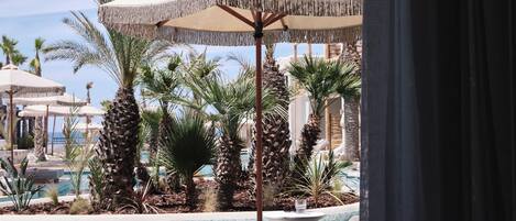Un área junto a la piscina con sillas de descanso, una sombrilla y palmeras.