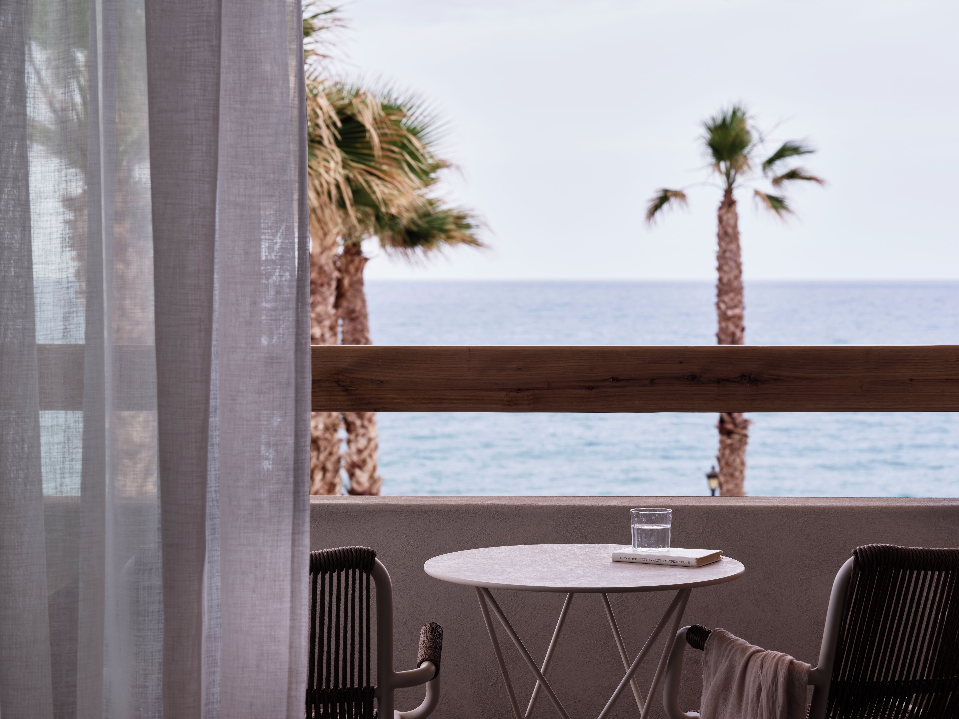 Un balcón con mesa y sillas, con vista al mar y palmeras.