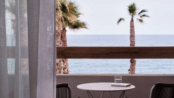 Un balcón con mesa y sillas, con vista al mar y palmeras.