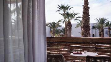 A terrace with wicker furniture, a table with a book and glasses, and palm trees in the background.