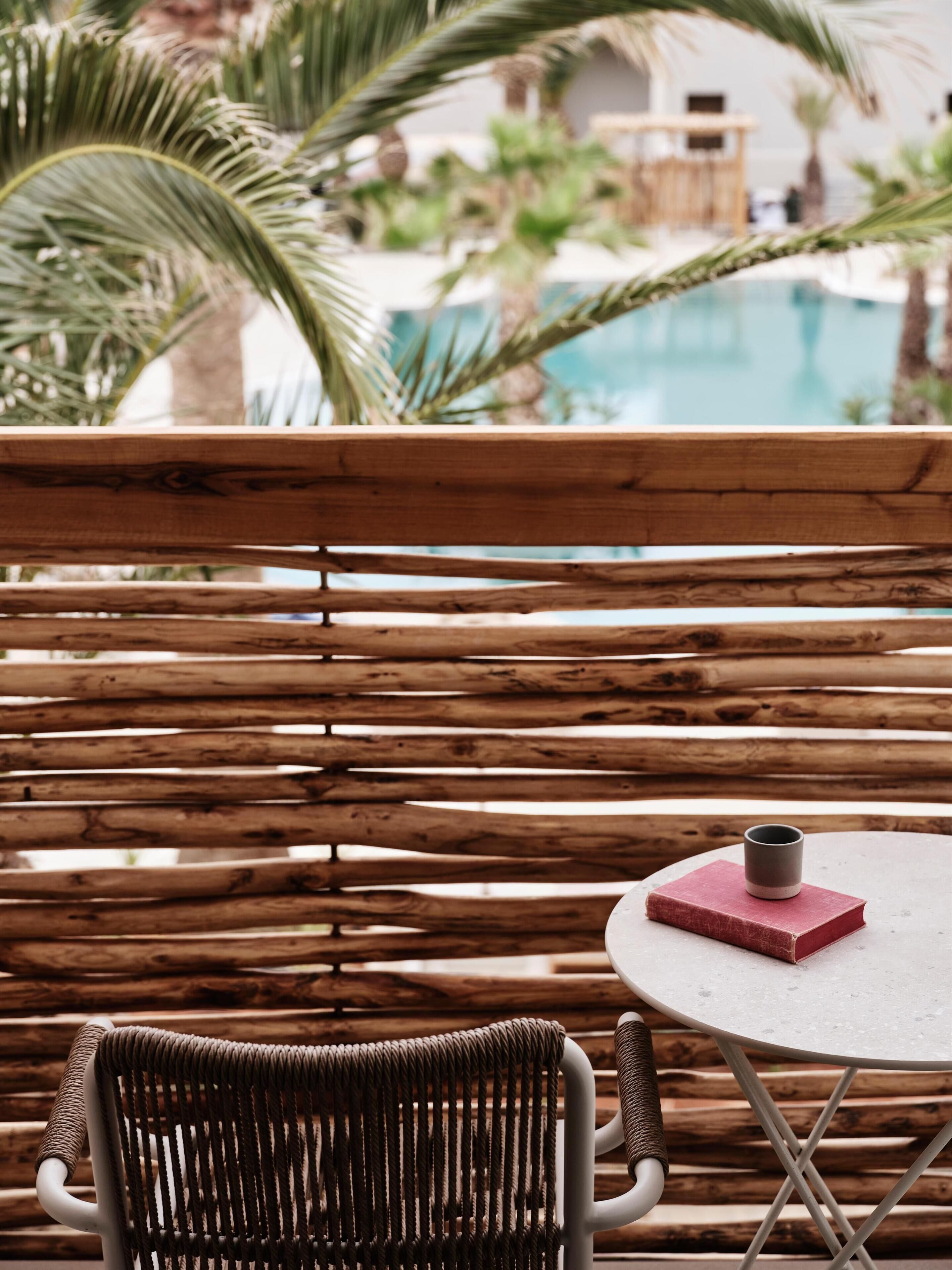 A wicker chair and a small round table with a book and a cup.