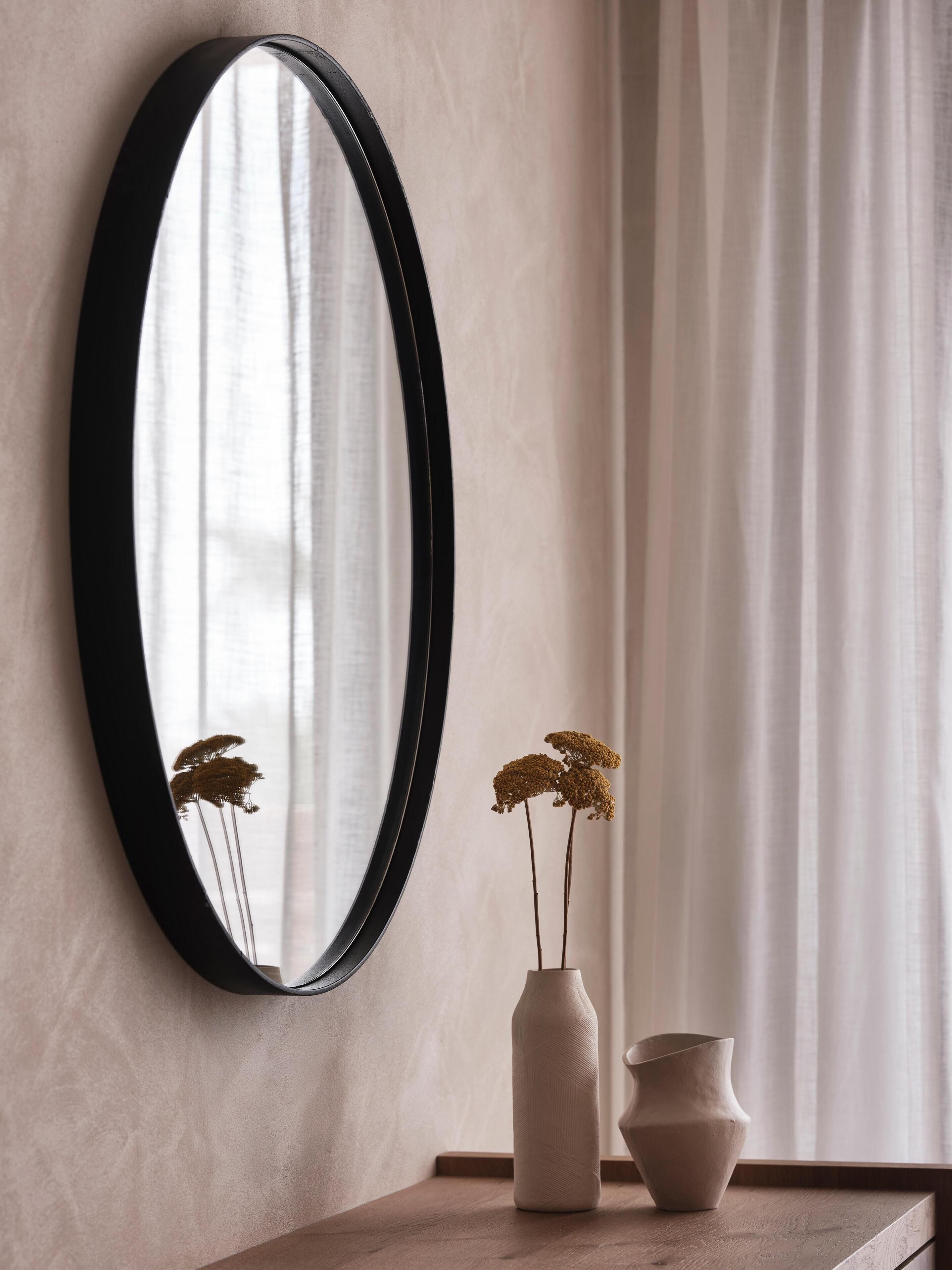 A mirror on a wall with a vase and a smaller pot on a wooden surface.