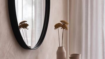 A mirror on a wall with a vase and a smaller pot on a wooden surface.