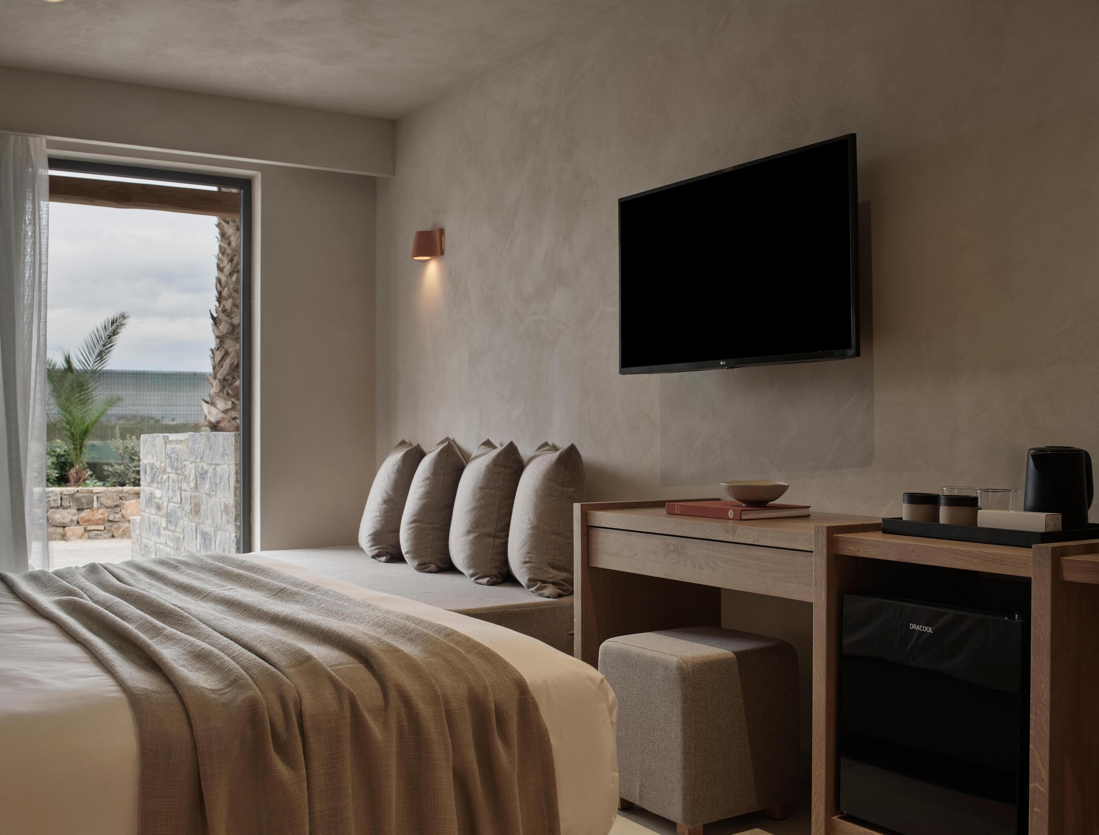 A modern hotel room with a large bed, a desk with a chair, a flat-screen TV, and a view of the outdoors.