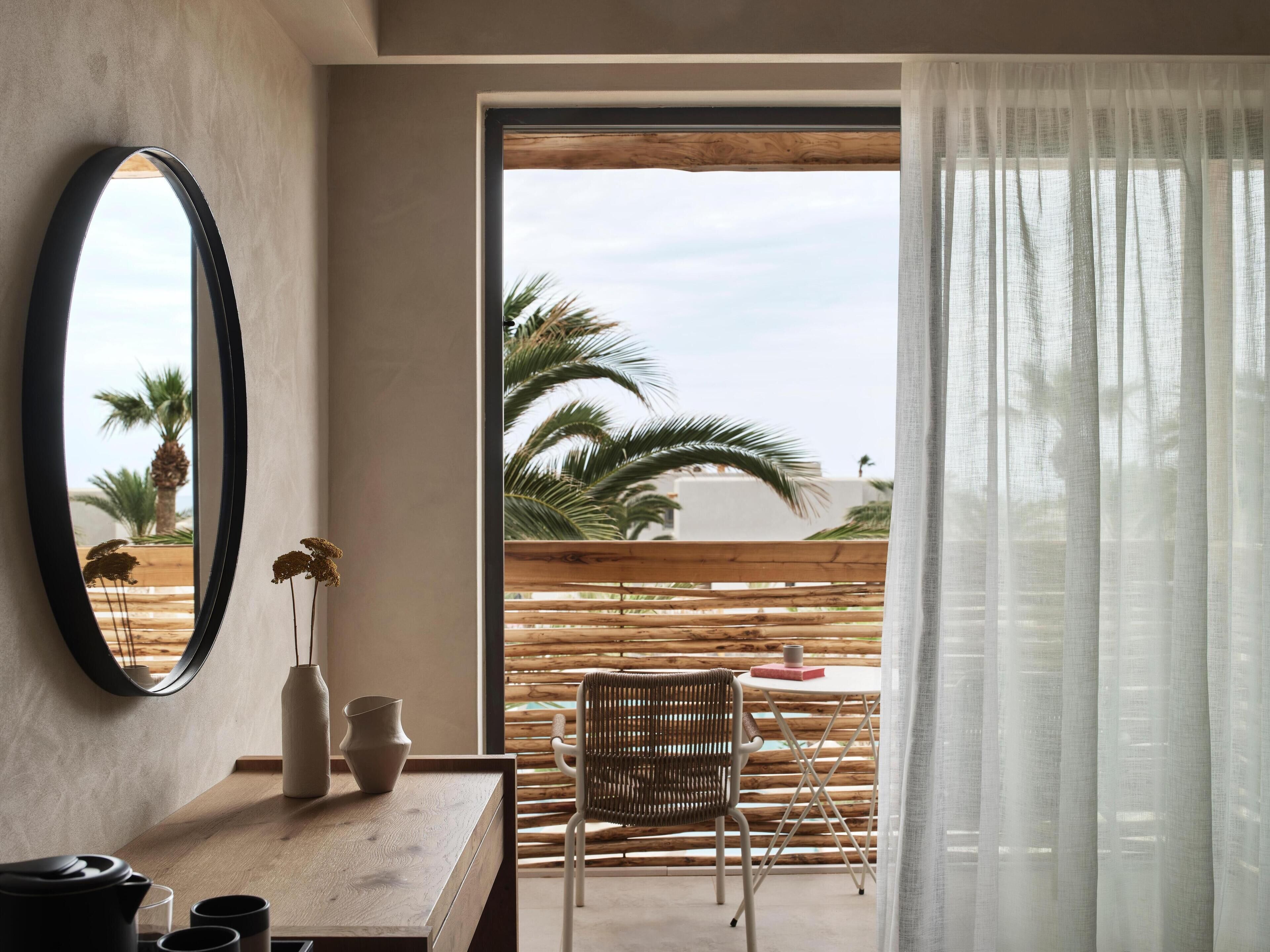 A modern room with a wooden desk, a mirror, and a view of palm trees through a large window.