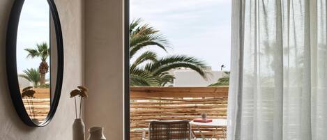 A modern room with a wooden desk, a mirror, and a view of palm trees through a large window.