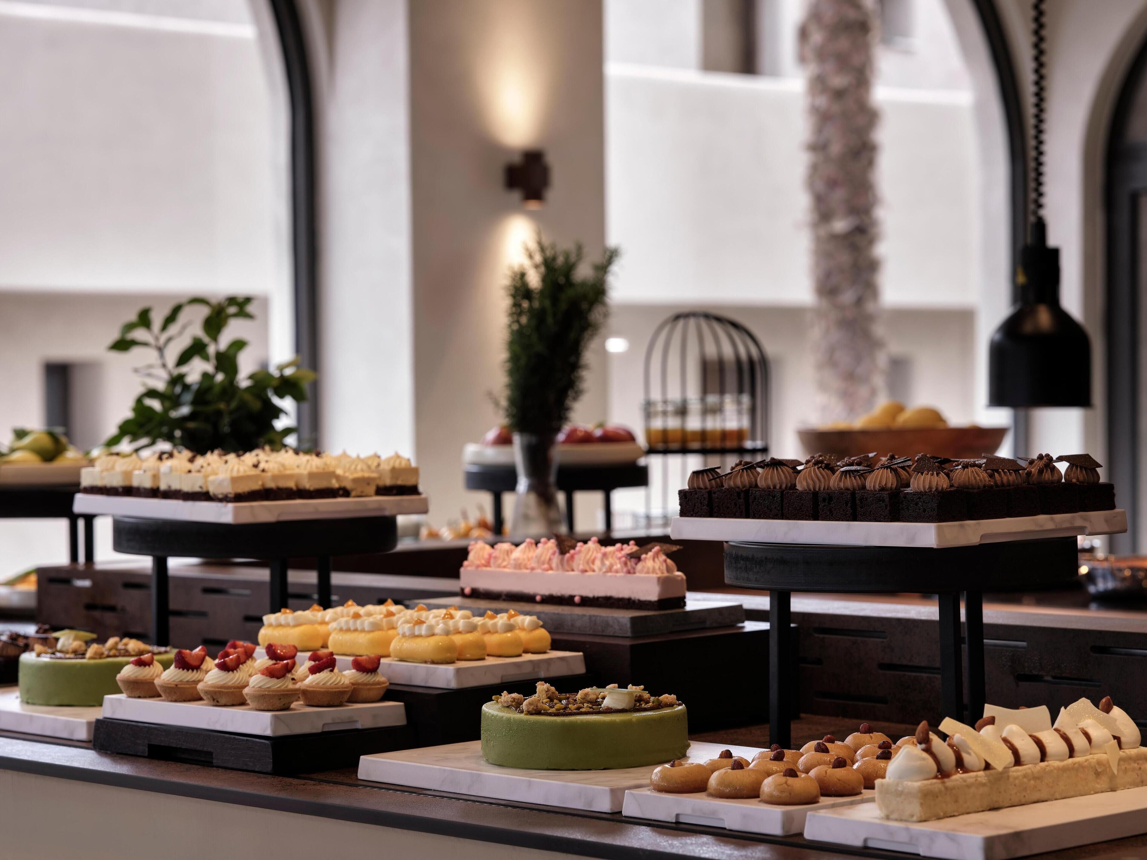 A variety of desserts displayed on tiered stands in a well-lit room with a modern interior design.