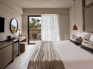 Habitación de hotel moderna con una cama grande, un escritorio con cafetera, un televisor y vistas a palmeras a través de la ventana.