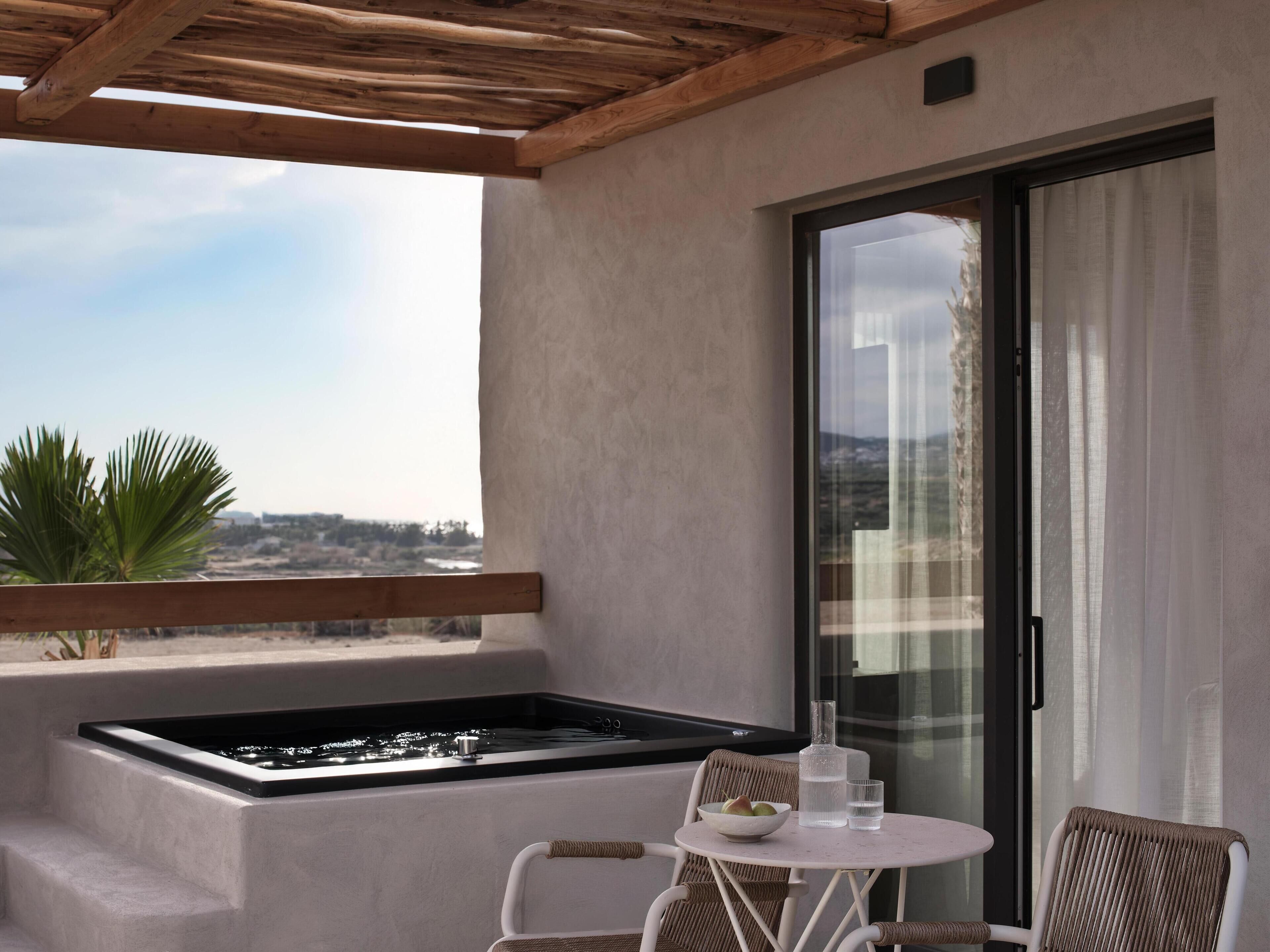 A balcony with a hot tub, a table with a bowl and glasses, wicker chairs, and a view of the landscape.