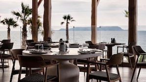 Un comedor con vistas al mar, con mesas redondas y sillas de mimbre.
