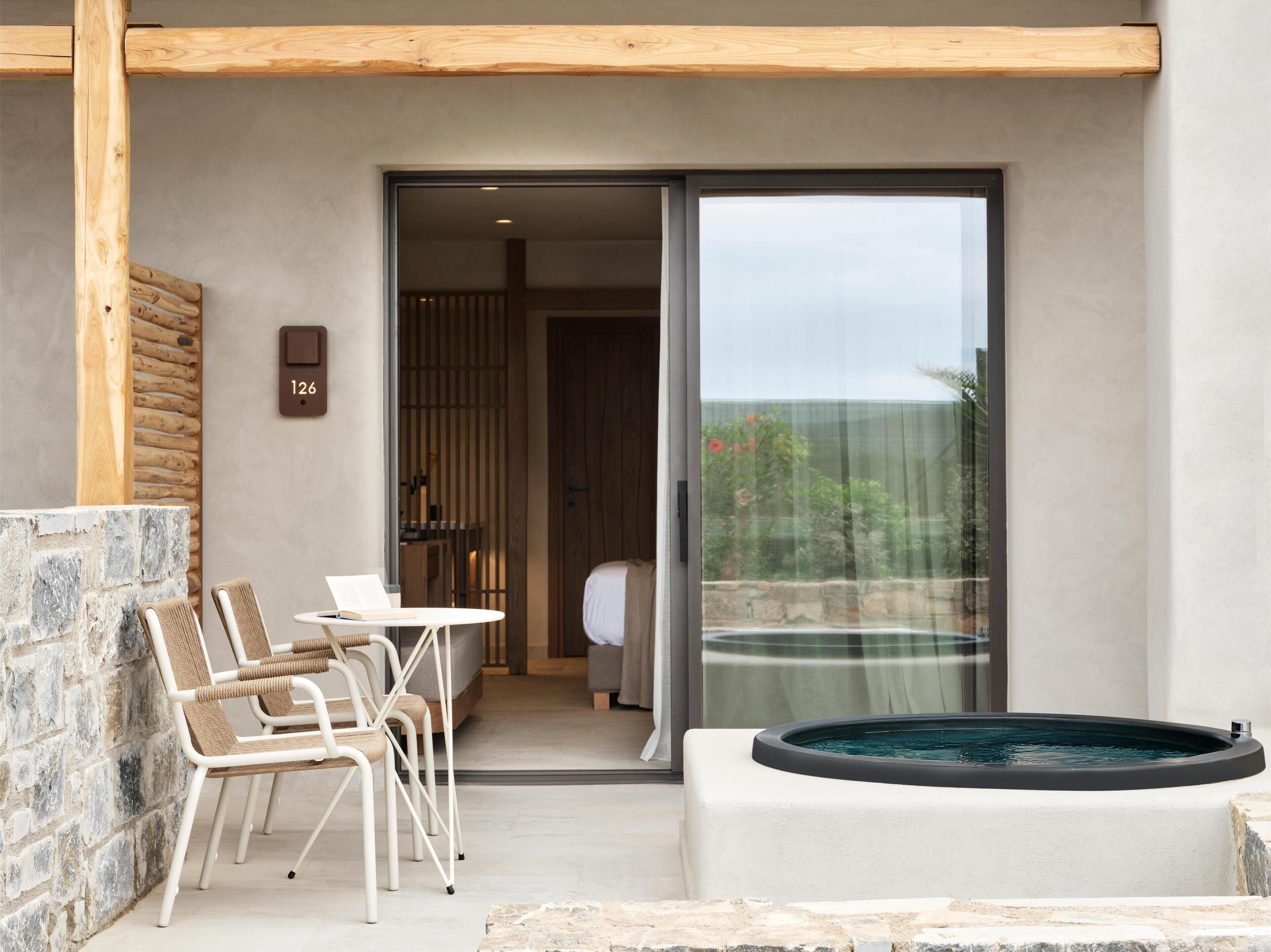 A modern outdoor seating area with a stone wall, a wooden ceiling, and a glass door leading to a room.