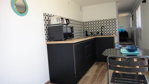 A compact kitchen with a microwave, kettle, and toaster on the counter, a sink, and a dining area with a table and chairs. - 2. Turquoise - HOME CASSIS - Maison Méditerranée (CASSIS)