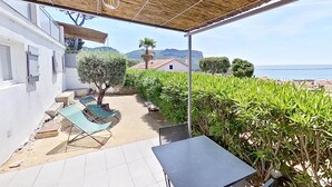 A covered outdoor area with a table and chairs, a view of the sea, and a building in the background. - 2. Turquoise - HOME CASSIS - Maison Méditerranée (CASSIS)