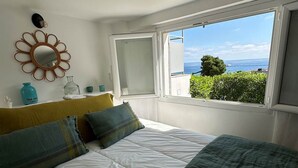 Ein Schlafzimmer mit einem Bett, einem Fenster mit Meerblick und einem an der Wand befestigten Spiegel.