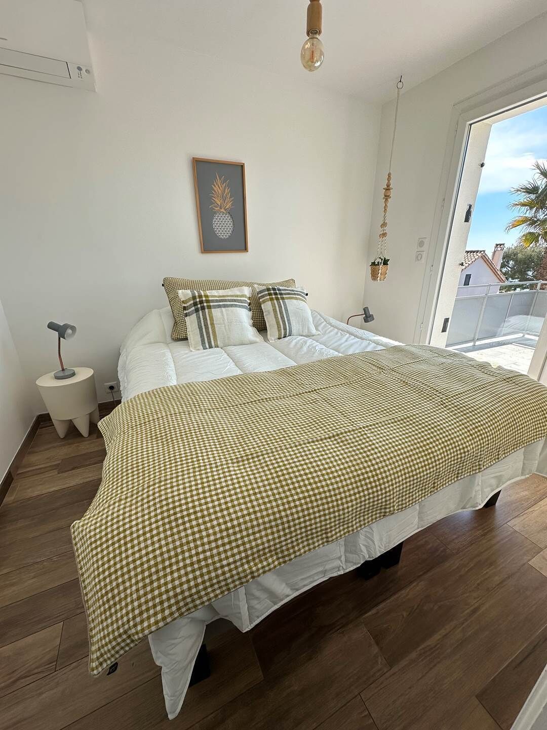 Ein Schlafzimmer mit einem großen Bett, einem kleinen Nachttisch, einer gerahmten Ananas-Kunst und Blick ins Freie.