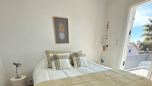 Un dormitorio con una cama grande, una mesita de noche pequeña, una obra de arte con una piña enmarcada y vistas al exterior.