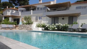 Una casa de dos pisos con piscina, muros de piedra y área de estar al aire libre.