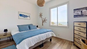 A bedroom with a bed, a nightstand, a dresser, a window with a view, and a wall decoration.