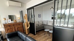 A modern living room with a black leather sofa, a wooden cabinet, and a large window offering a view of the outdoors.