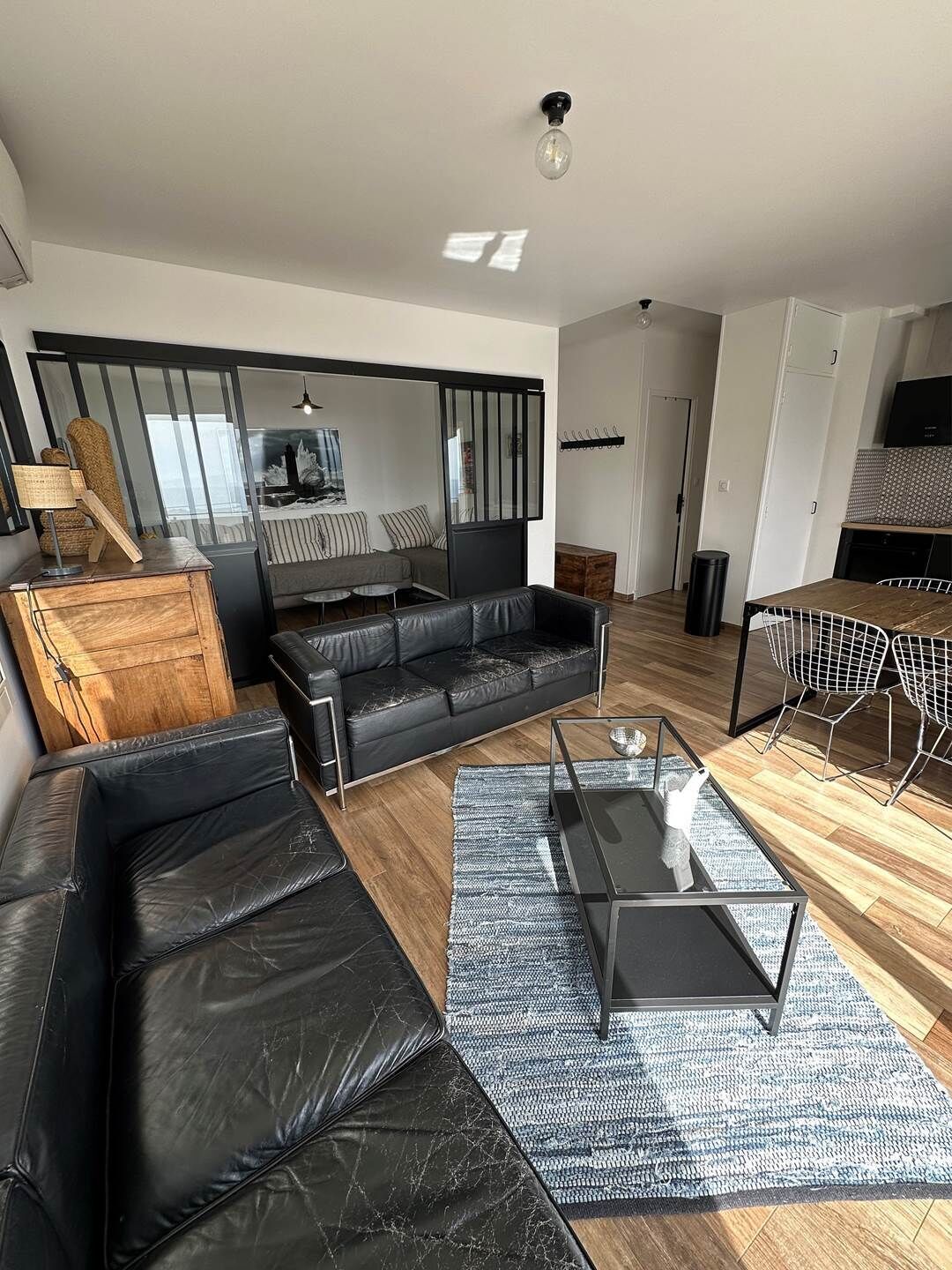 Un salon moderne avec un canapé en cuir noir, une table basse en verre et un coin repas doté d’une chaise en métal.