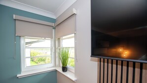 Una habitación con dos ventanas, una planta en maceta y una barandilla de madera.