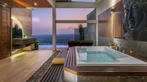 A modern bathroom with a large bathtub, a view of the mountains, and a Buddha statue.