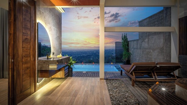 A modern interior with a view of a sunset over a pool, wooden flooring, and a seating area.