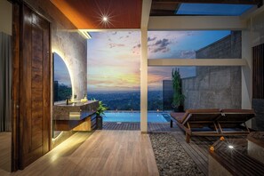 Een modern interieur met uitzicht op een zonsondergang boven een zwembad, houten vloeren en een zithoek.