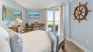 Un dormitorio con cama, escritorio, silla, ventana con cortinas y una rueda de barco en la pared.
